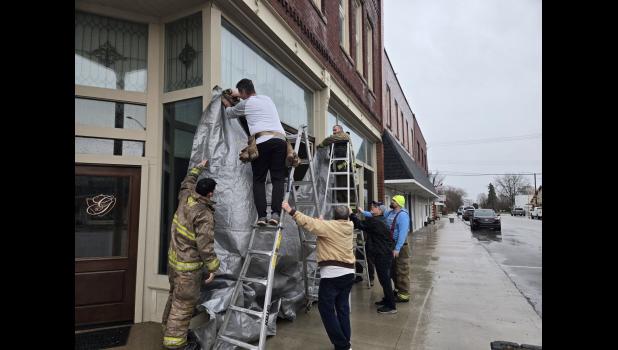 Photo provided. Volunteers and firemen help put a tarp in front of a blown in window in downtown Francesville on March 30.