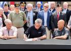 Gov. Eric Holcomb (seated, center) signs legislation co-authored by State Rep. Doug Gutwein (R-Francesville) (first row standing, far left) providing tax relief to many Hoosier veterans Monday, Aug. 5, at the Indiana State Fair in Indianapolis. The new law will phase in a full income tax exemption for military retirement pensions over four years, helping to support the hard-earned benefits of Hoosier veterans.